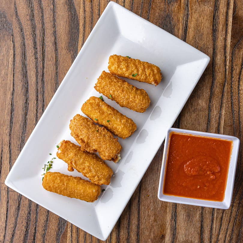 Six golden-brown mozzarella sticks with herbs on a white rectangular plate, with a side of marinara sauce.
