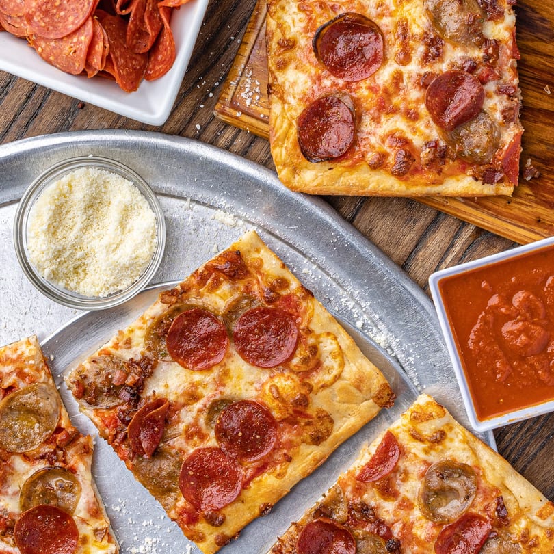 Square-cut pepperoni and sausage pizzas with sides of marinara, parmesan, and extra pepperoni.
