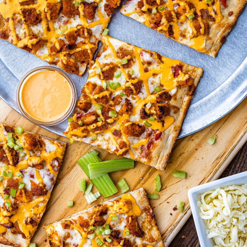 Buffalo chicken flatbread slices with ranch drizzle, celery, and a side of ranch dressing.