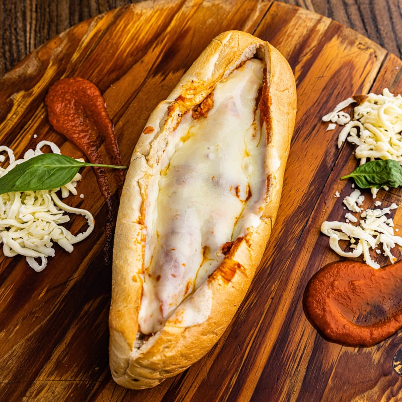 Meatball sub with melted cheese and marinara sauce on a wooden board with shredded mozzarella and basil.