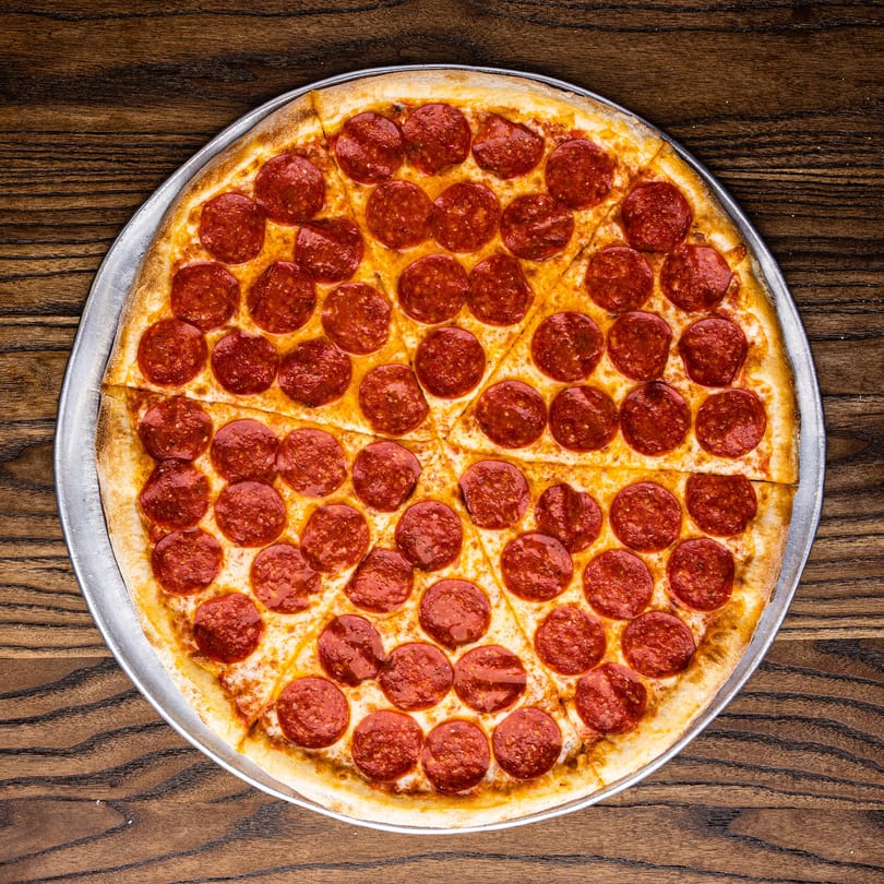 A whole pepperoni pizza, sliced into eight pieces, on a metal tray over a wooden table.