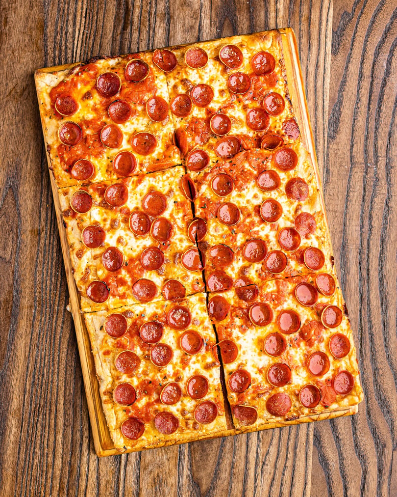 Rectangular pepperoni pizza, cut into squares, on a wooden board.