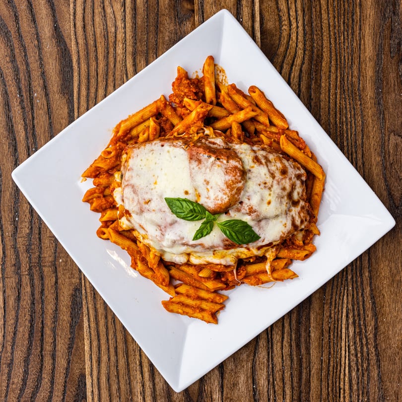 Chicken parmesan with penne pasta and marinara sauce, topped with melted cheese and basil.