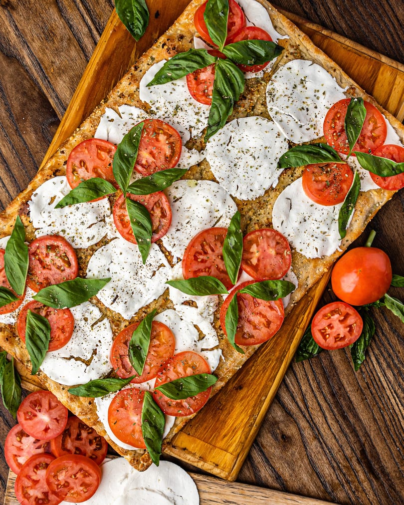 Caprese flatbread with fresh mozzarella, sliced tomatoes, and basil on a wooden board.